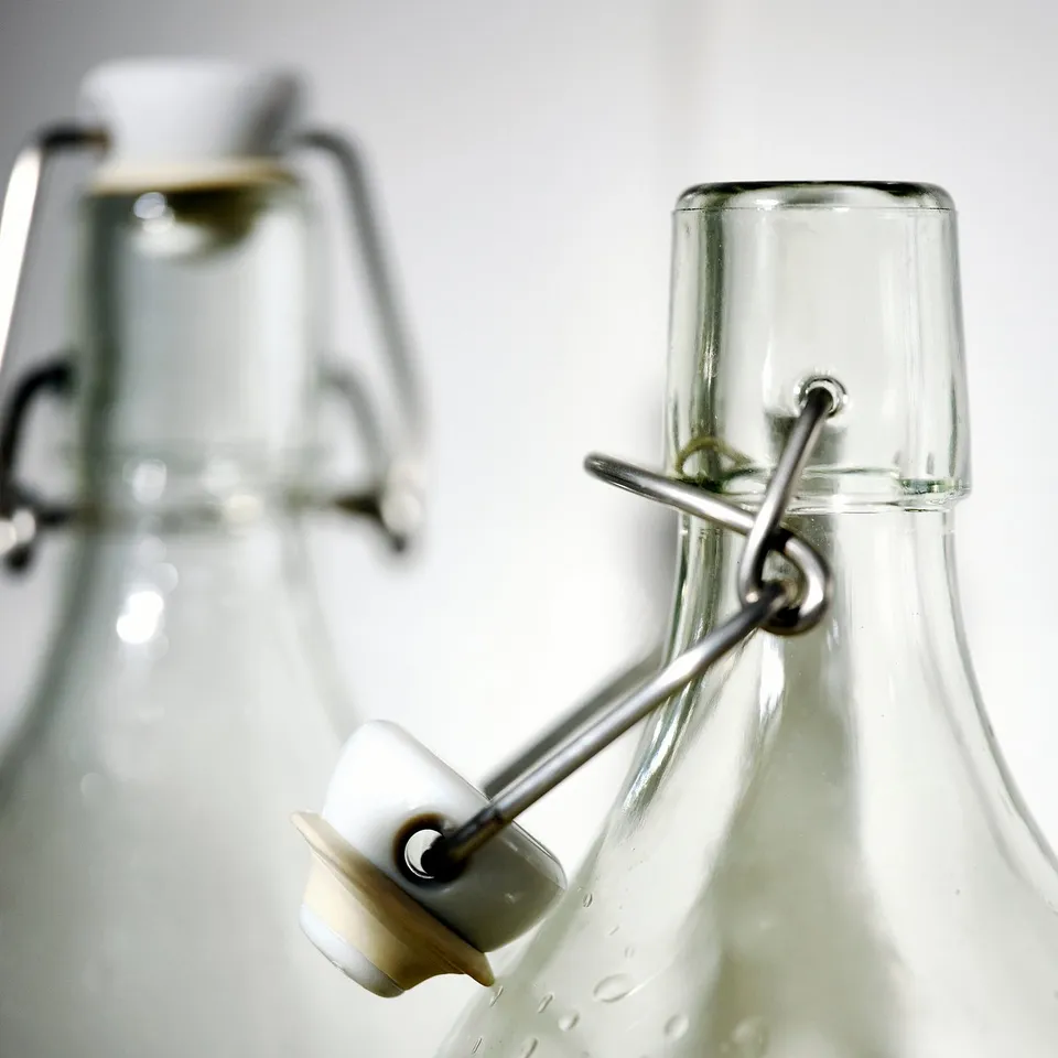 Two transparent glass bottles with airtight metal clamp lids, designed for storing liquids or solids, effectively sealing contents.