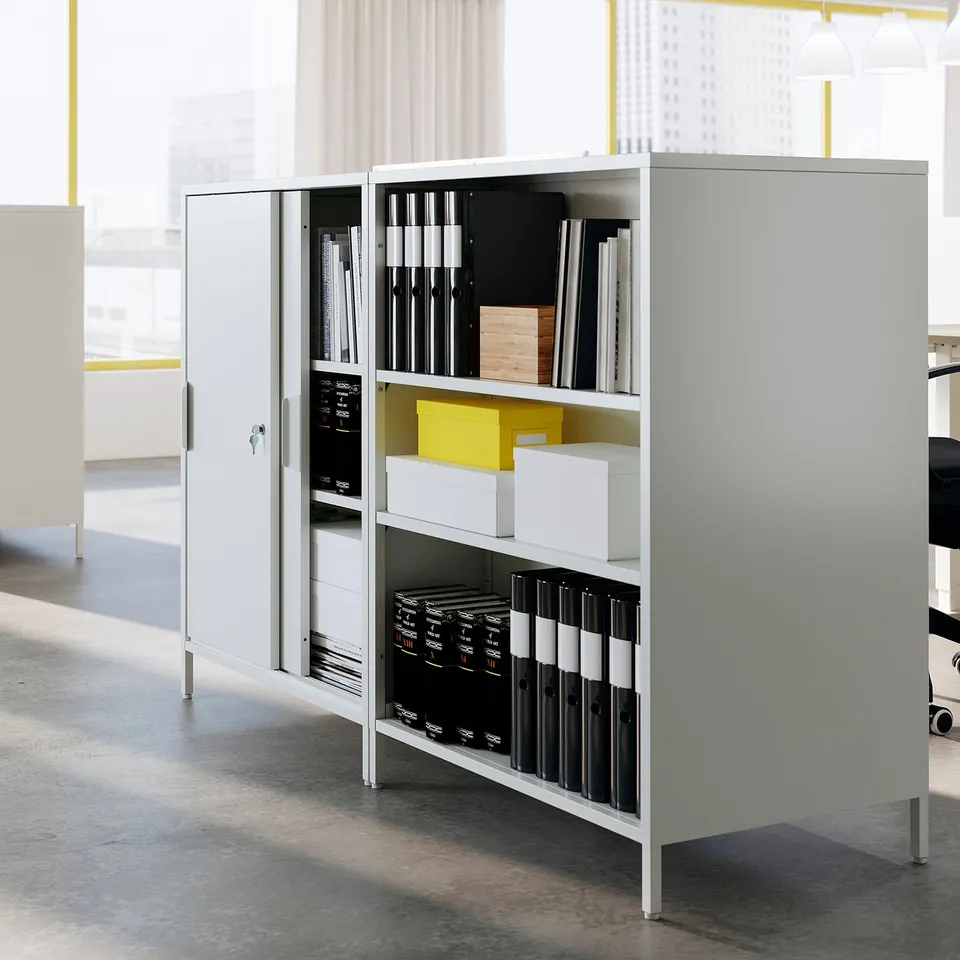 A white TROTTEN double-sided office cabinet with sliding doors, storing binders and boxes, acting as a room divider.