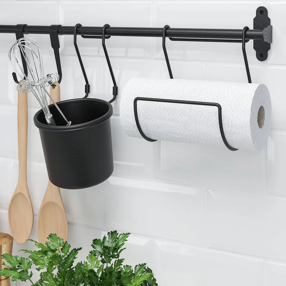 Kitchen storage system: paper towel, utensil holder, and hooks on white tiled wall.