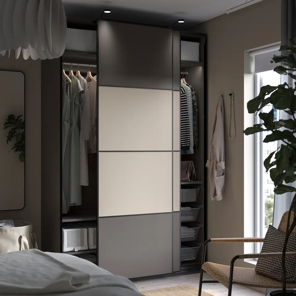 Modern bedroom with PAX wardrobe. Wardrobe sleek black and white panels, hanging clothes, shelves, and a wicker chair.