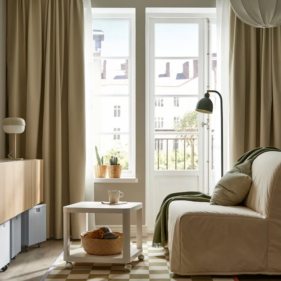 Cosy living area with large window, beige sofa, mobile side table, and lamp.