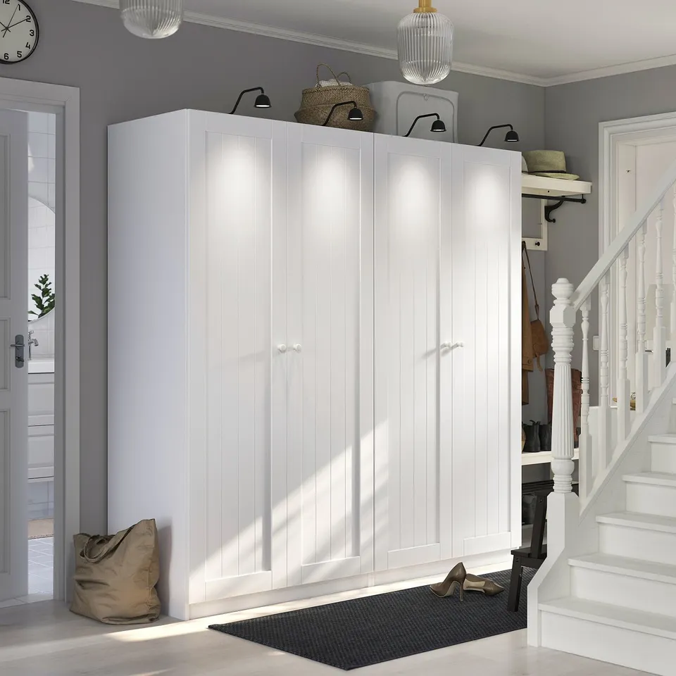 Large white PAX wardrobe in entryway with stairs and door. Sits above black mat, surrounded by decor.
