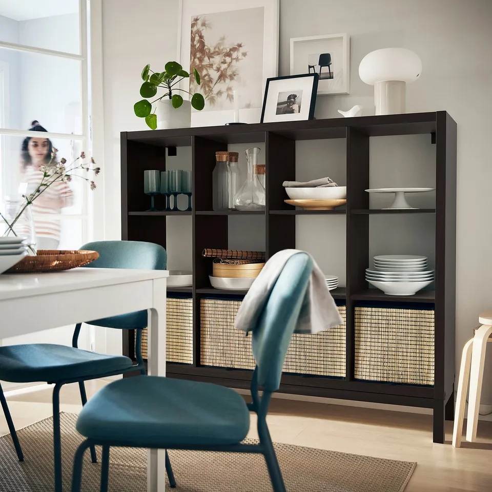 Modern dining room with KALLAX shelves, decor, and blue chairs by a large window.