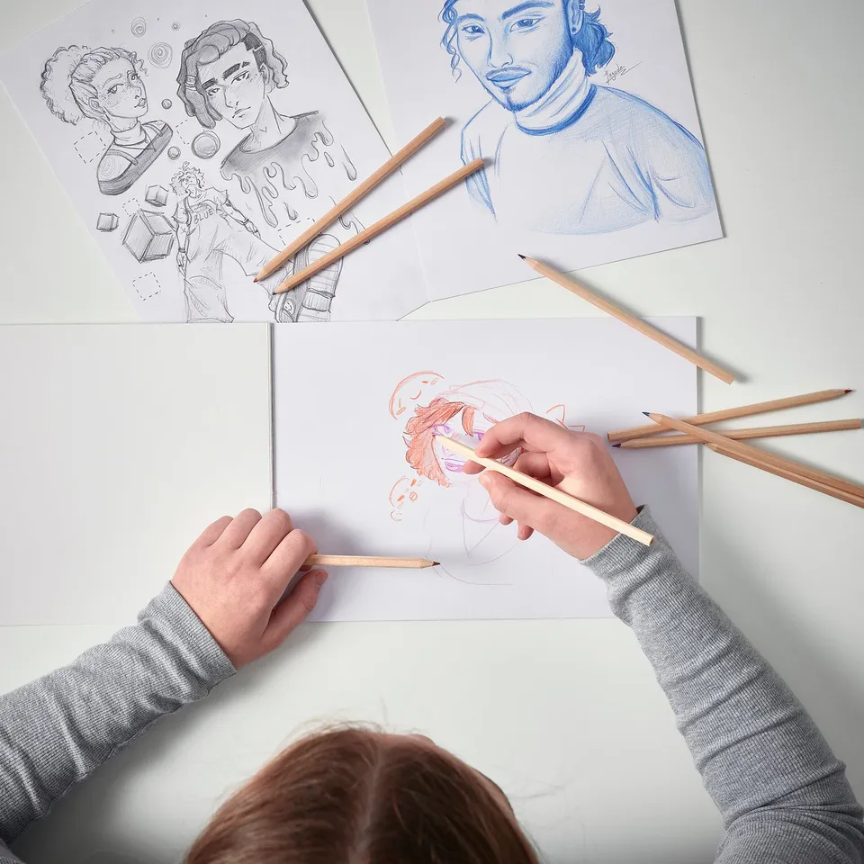 Two people draw on paper with SOLFÅGEL pencils, showcasing detailed artwork and rich colours.