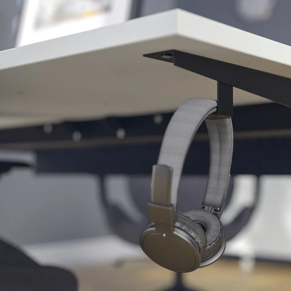 Black headphones hang on metallic desk hook, showcasing a functional feature of the MITTZON underframe for organising workspace accessories.