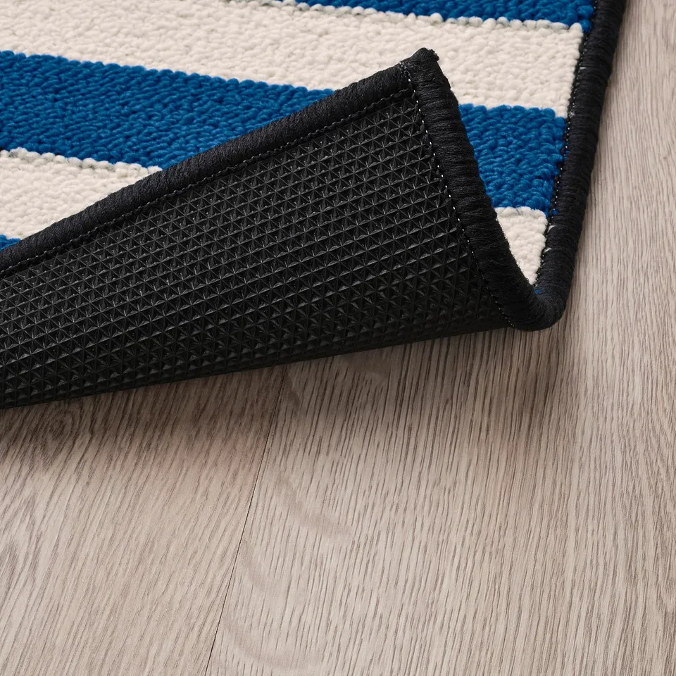 Blue and black striped rug corner with black non-slip backing on wooden floor.