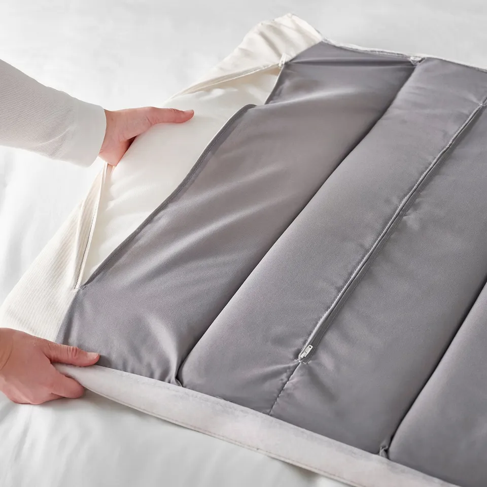 A person is placing a grey bed sheet onto a modern bed frame with an adjustable headboard.