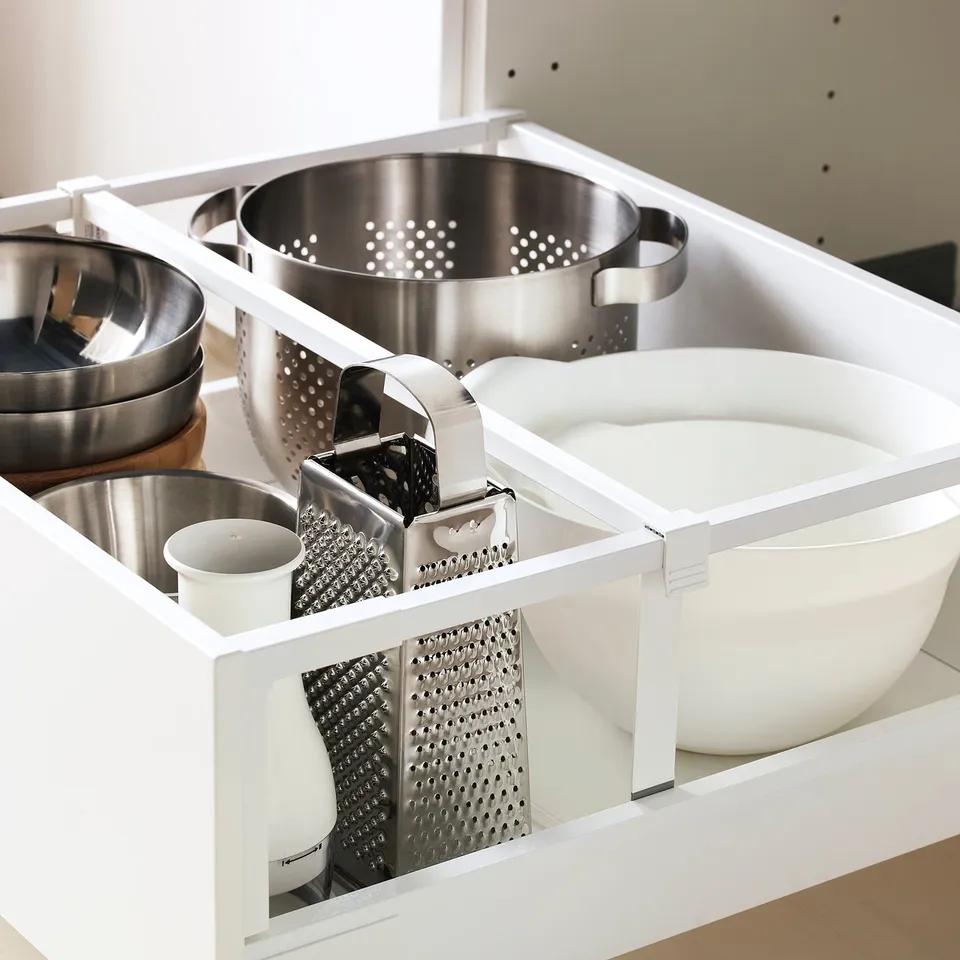 Kitchen drawer organiser holding pots, bowls, and graters. White frame with adjustable compartments and full-extension glide.