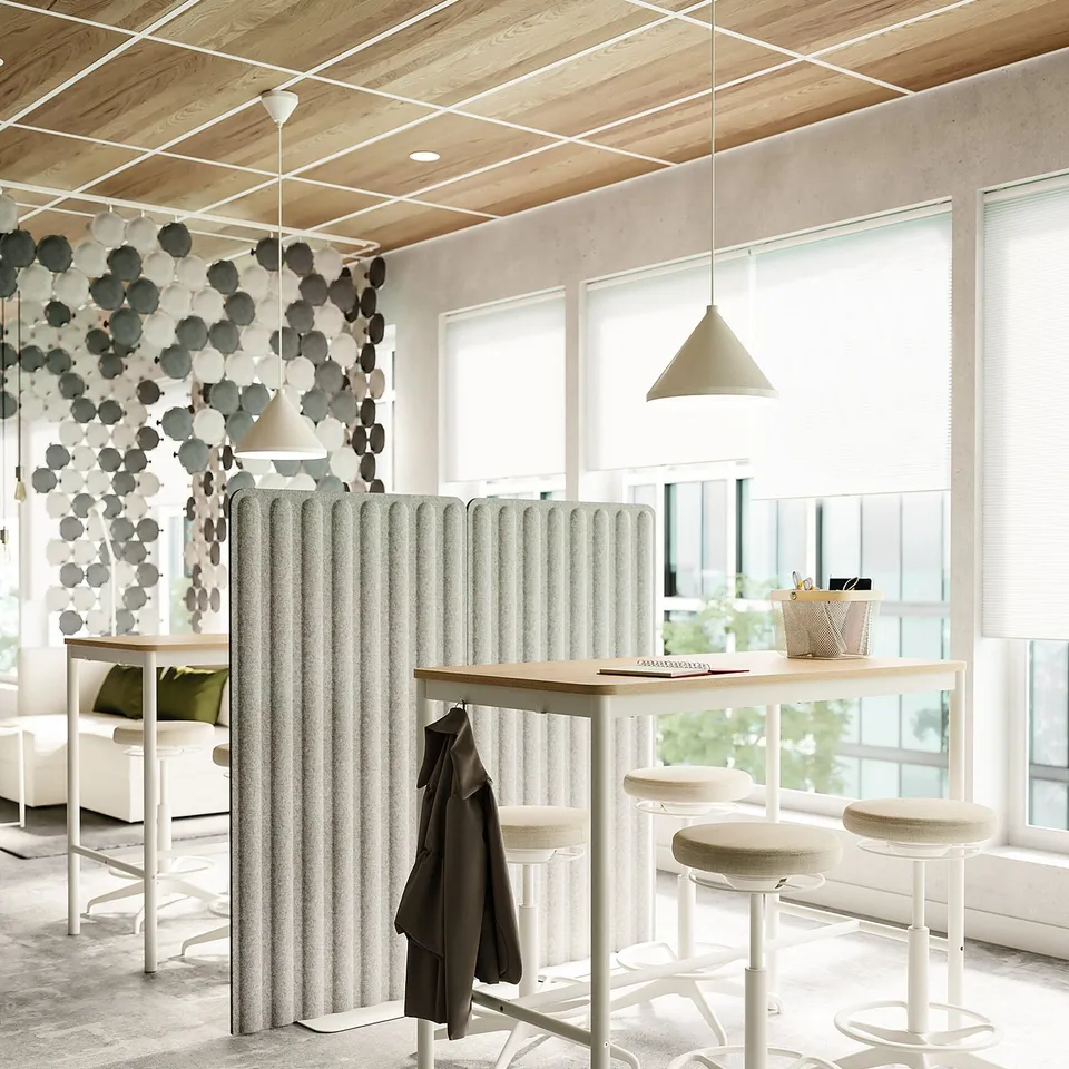 Modern office space with high tables, white stools, and a unique sound-absorbing wall panel. Wooden ceiling, large windows, and hanging lights.