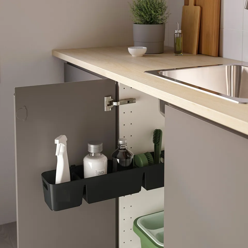Black organiser slides out from under kitchen sink, holding cleaning supplies like sponges, bottles, and brushes.