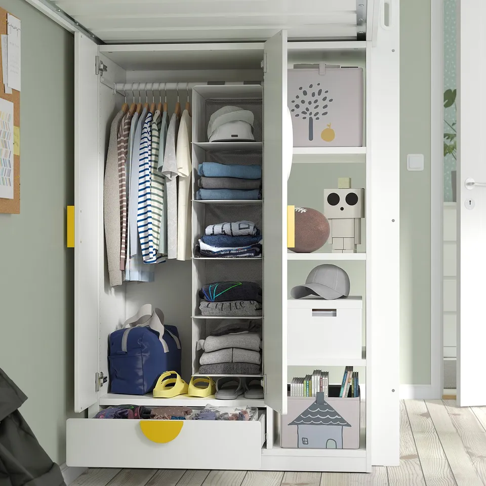 White IKEA smastad kids loft bed with integrated wardrobe, desk, and shelves for clothes, books, and toys.