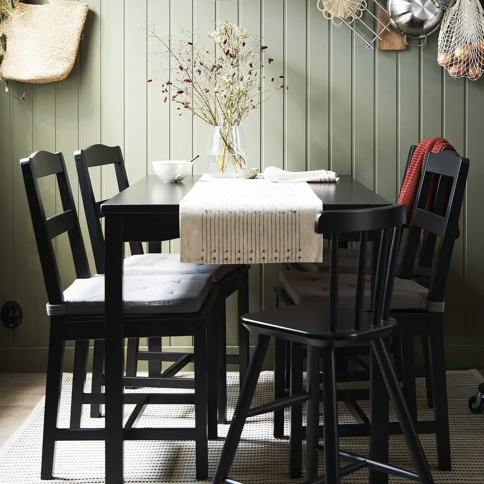 HÄGERNÄS black dining set with floral centrepiece on table, four matching chairs, green vertical wall panel.