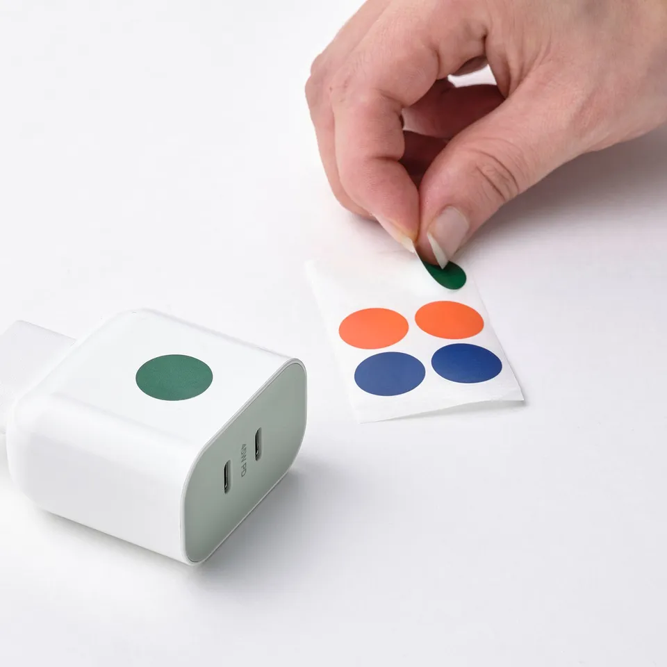 Hand peeling off coloured sticker from SJÖSS 45w charger, showing personalization feature.