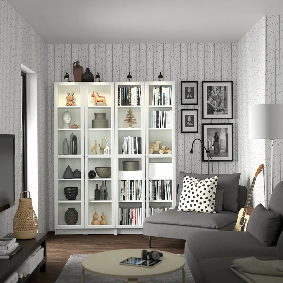 Modern living room with grey couch, white BILLY bookcases filled with books and decor, polka dot pillow, wooden coffee table, and guitar.