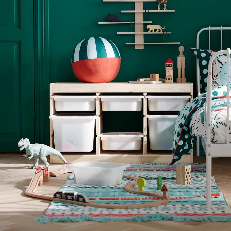 Vibrant kids room with green walls, wooden toy shelf, dinosaur toy, colourful rug, and wooden storage unit with drawers.