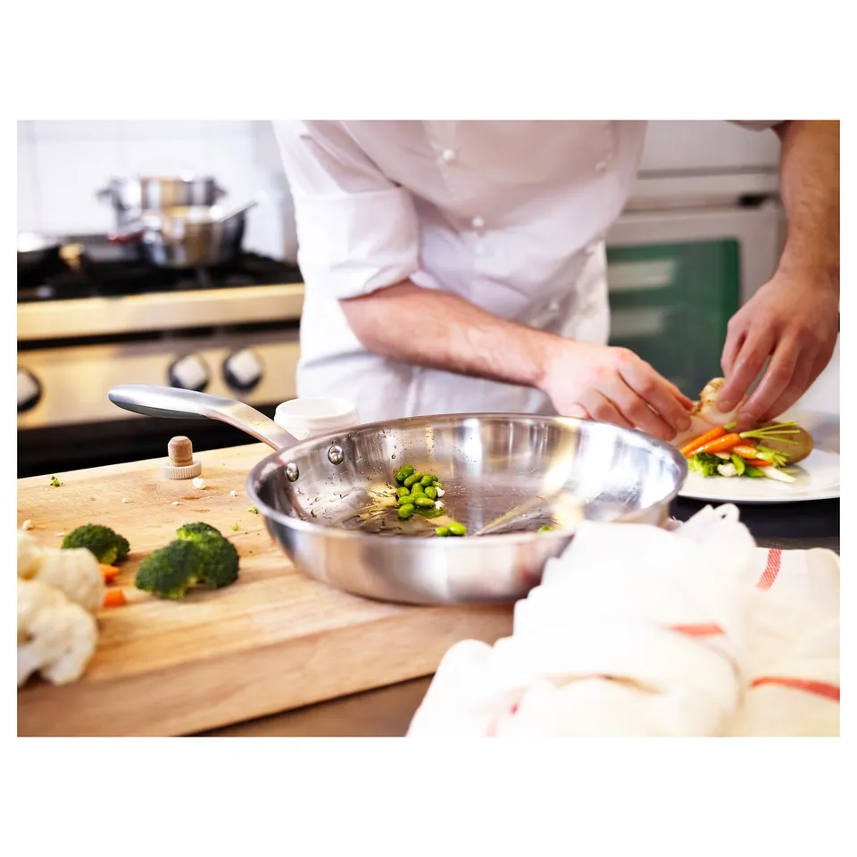 Chef cooking in kitchen with SENSUELL pan. Aluminium core for even heat, sautéing veggies.