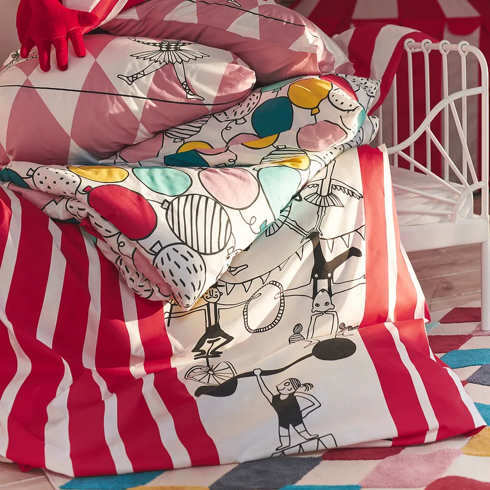 Circus-themed kids bedding: white bed with red-striped blanket, colourful characters, and red gloves.