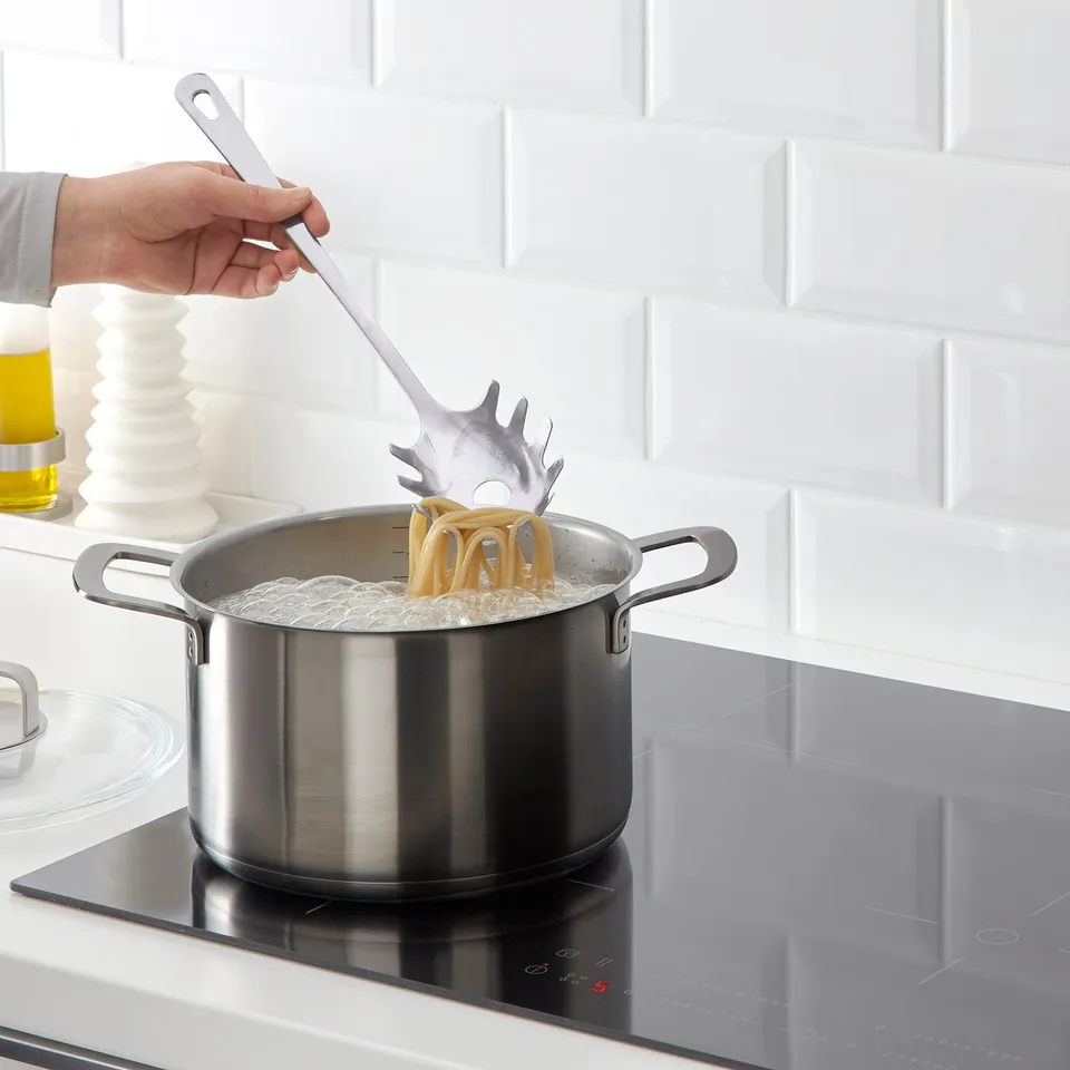 Person cooking pasta using a spaghetti server from the GRUNKA set on a stove.