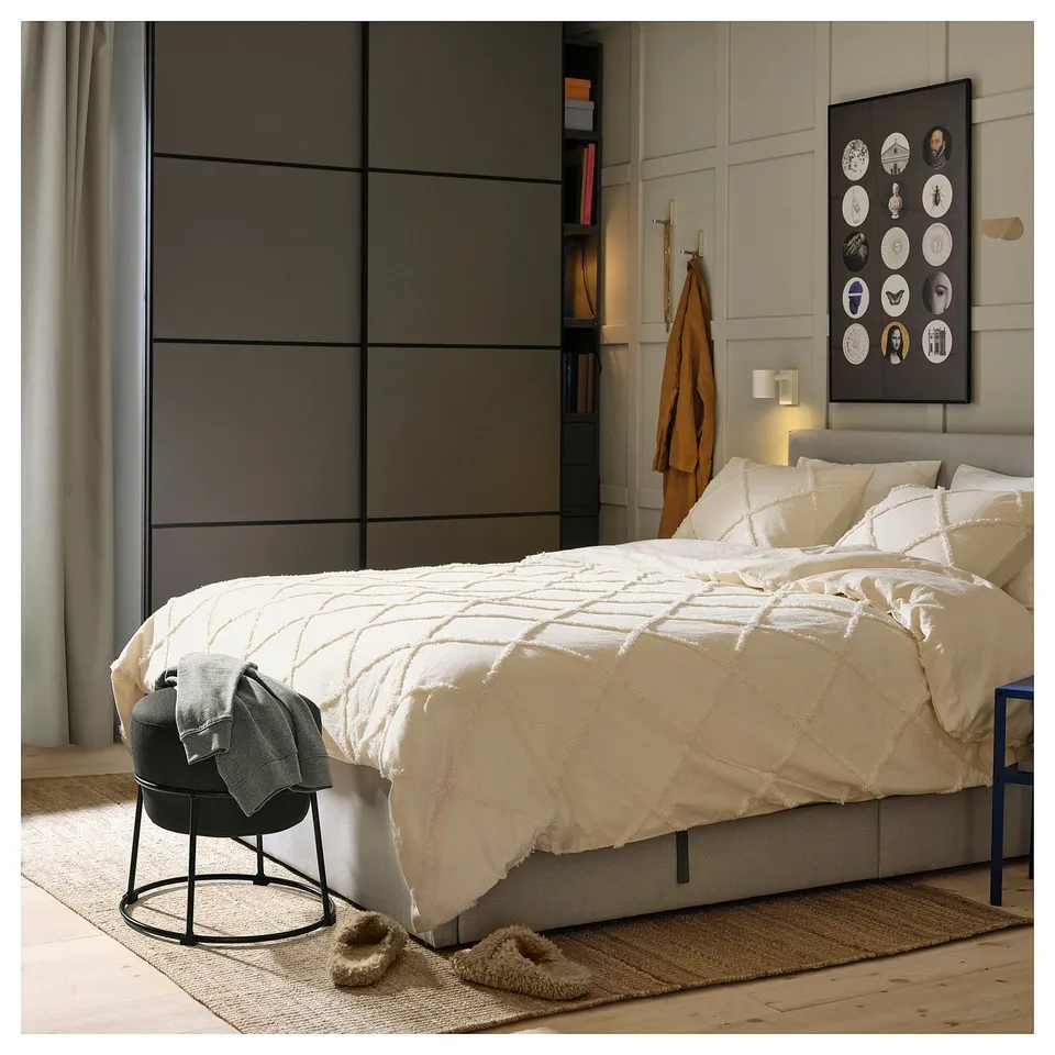 Modern bedroom with white bed, grey chair, plush slippers, and art wall.