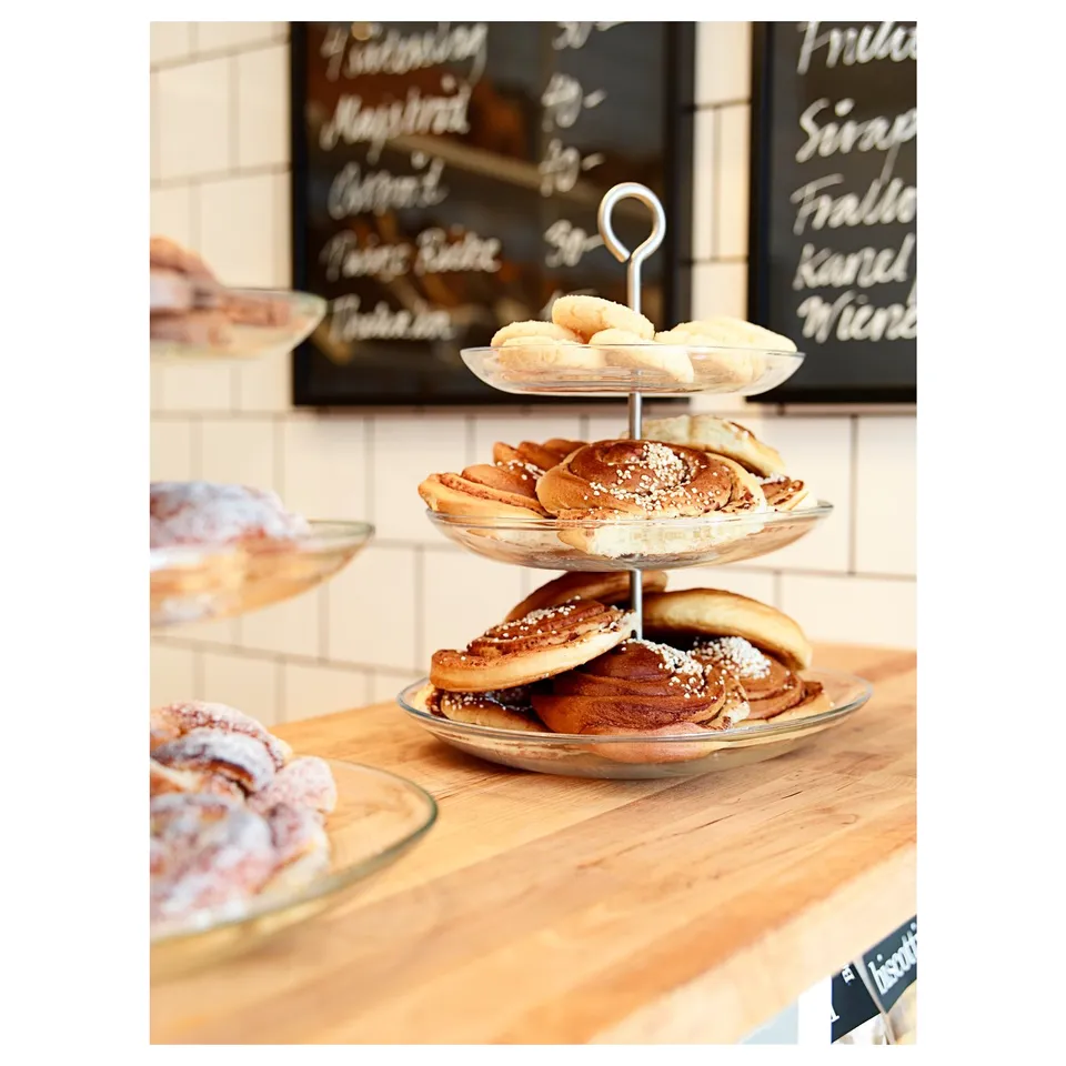 Three-tier glass serving stand with pastries. Modern, practical, and airy design for finger food. Stainless steel handles.