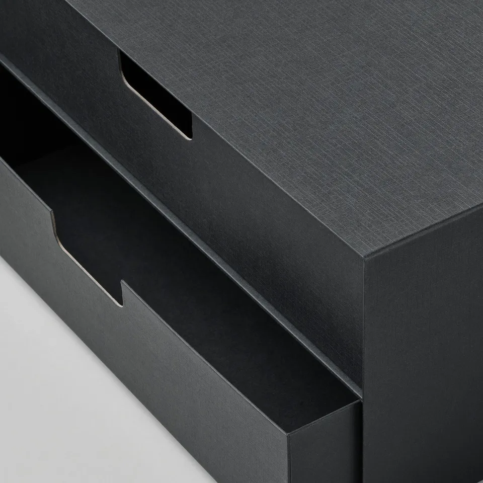 Black mini chest of drawers with three sections, textured surface, and cut-out handles. Sturdy and neatly designed for organising items.