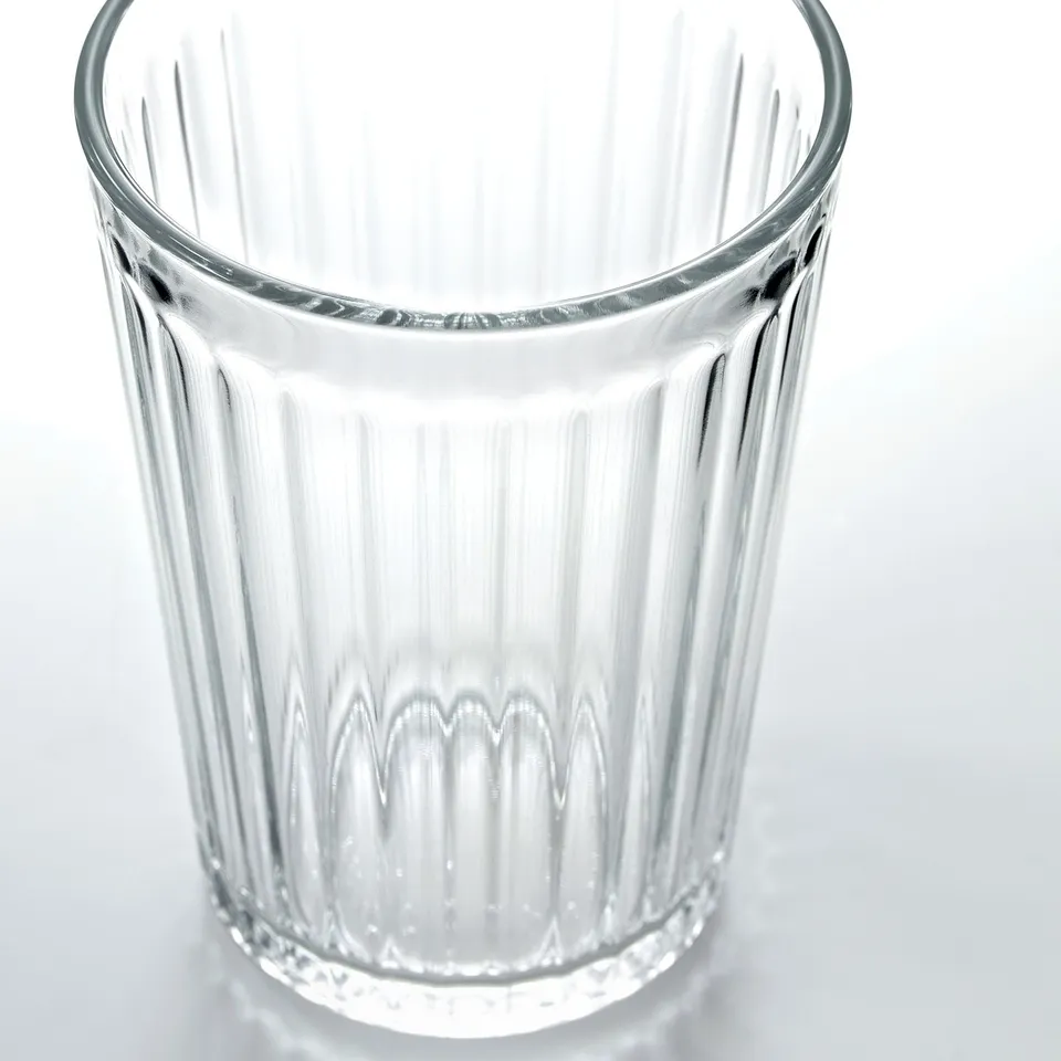 Clear, empty glass with vertical ridges, standing alone on a white surface. Simple, elegant design.