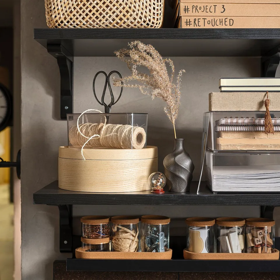 Dark brown shelves with various office supplies and decorative items, including baskets, scissors, and a vase with dried plants.