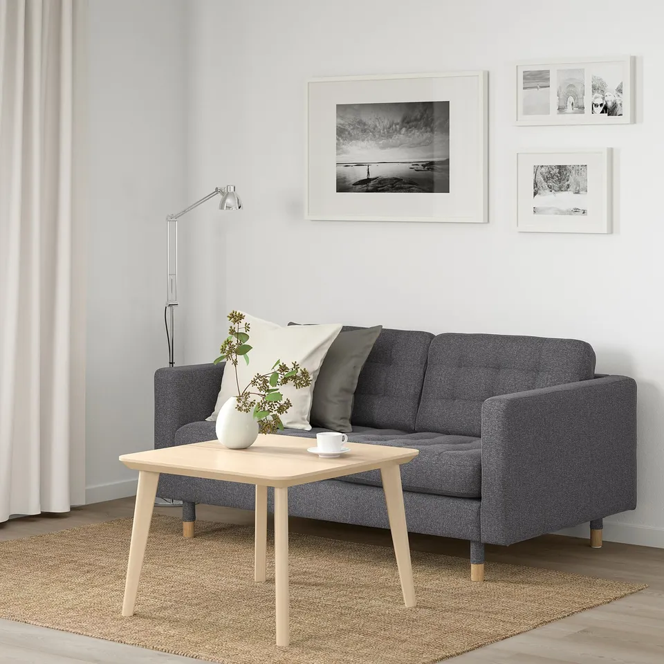 A minimalist living room with a LANDSKRONA grey sofa, high resilience cushions, wooden coffee table, black & white photos, floor lamp, and rug.