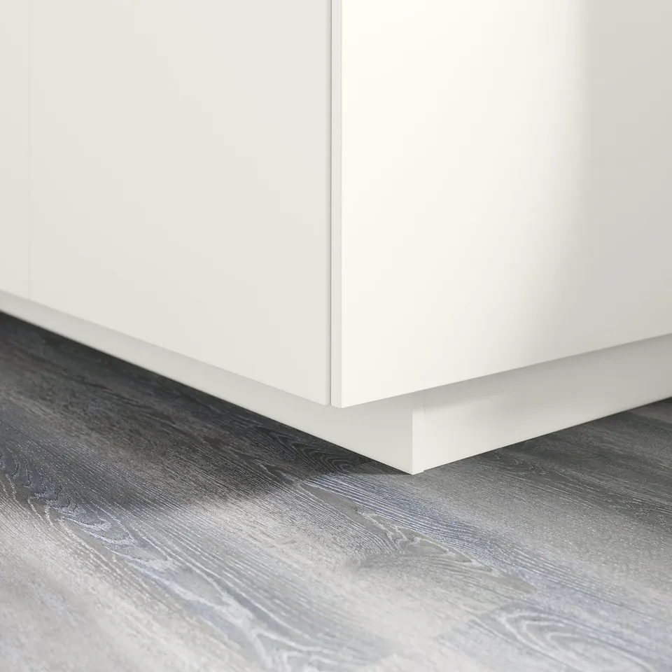 White kitchen cabinet leg attached to grey wood floor.