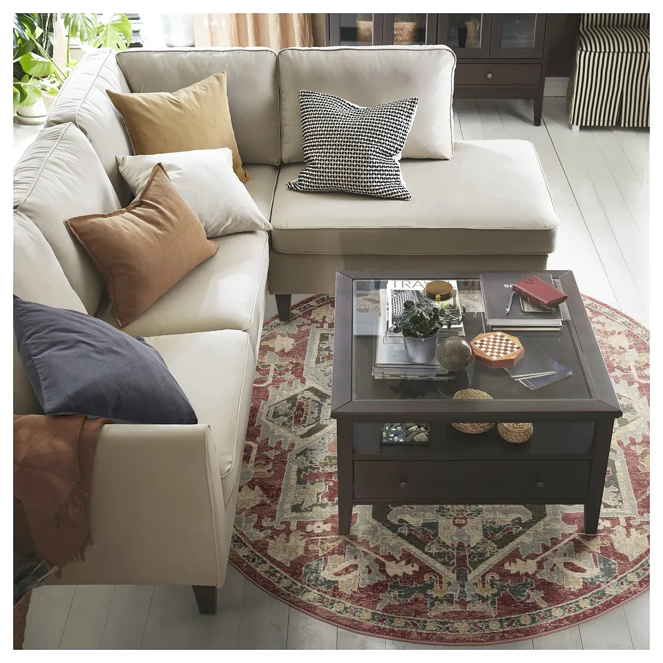 Modern living room with beige sectional, dark coffee table, and colourful round rug with patterns.