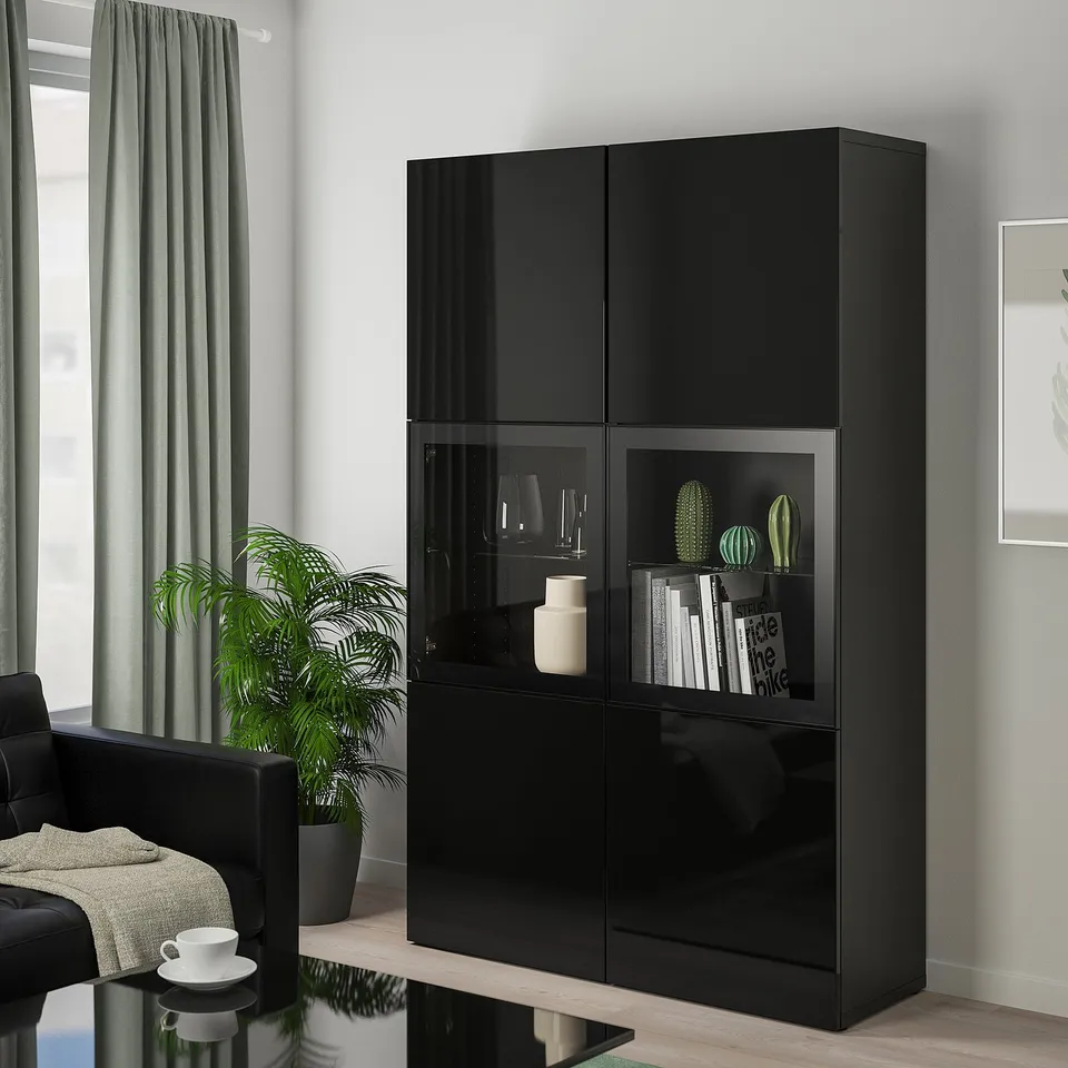 Modern living room with black BESTÅ unit, glass doors, green curtains, black chair & white blanket.