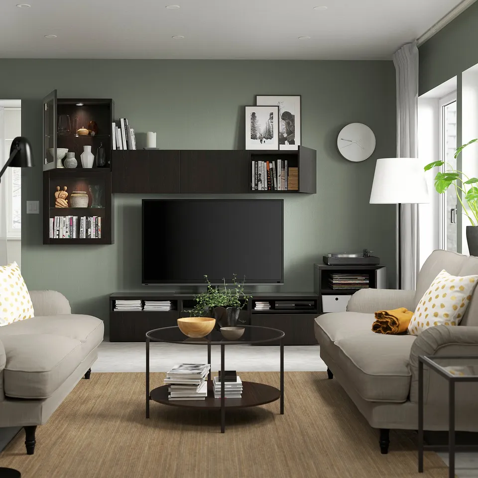 Modern living room with green walls, tv unit, grey sofa, and coffee table with books and bowls.