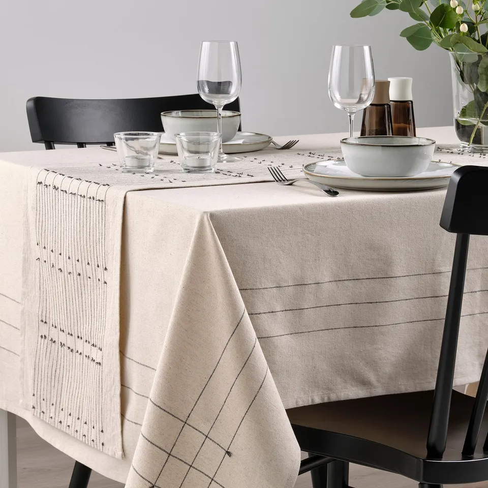 Table set with VÅRARV runner, plates, bowls, glasses on chairs, grey wall background.