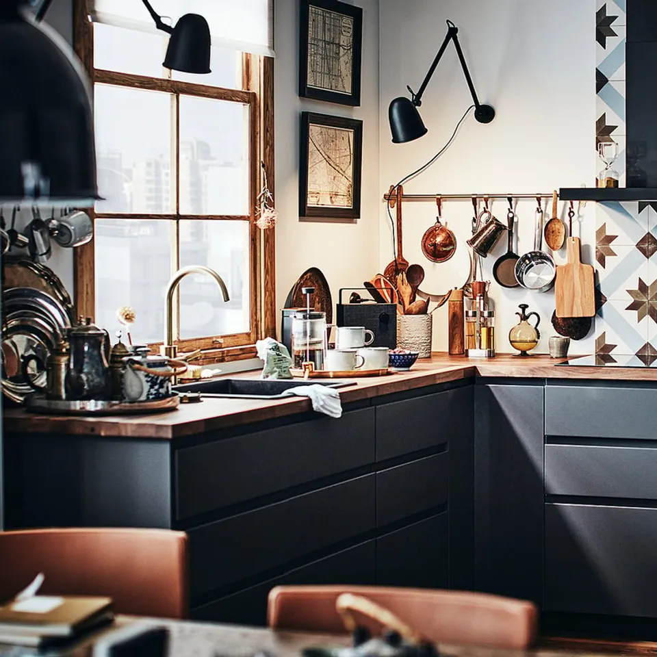 Modern kitchen with KARLBY dark wooden countertops and black cabinets. Various utensils hang above the sink. A window lets in natural light.