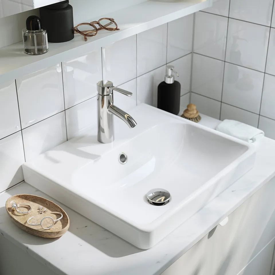 White rectangular sink with chrome tap, soap dispenser, and jewellery tray on counter. Tiles in the background.