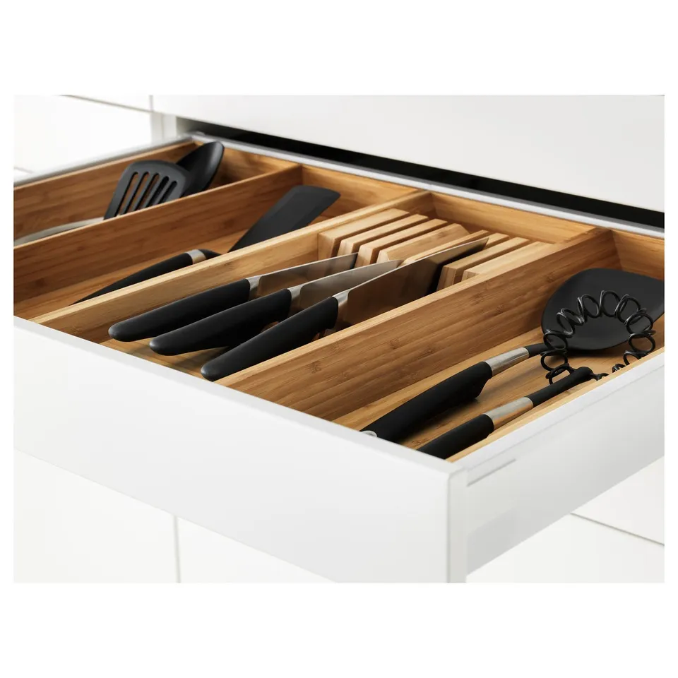 Wooden knife organiser in kitchen drawer, holding black-handled knives, utensils, and cutting boards, with self-closing drawers.