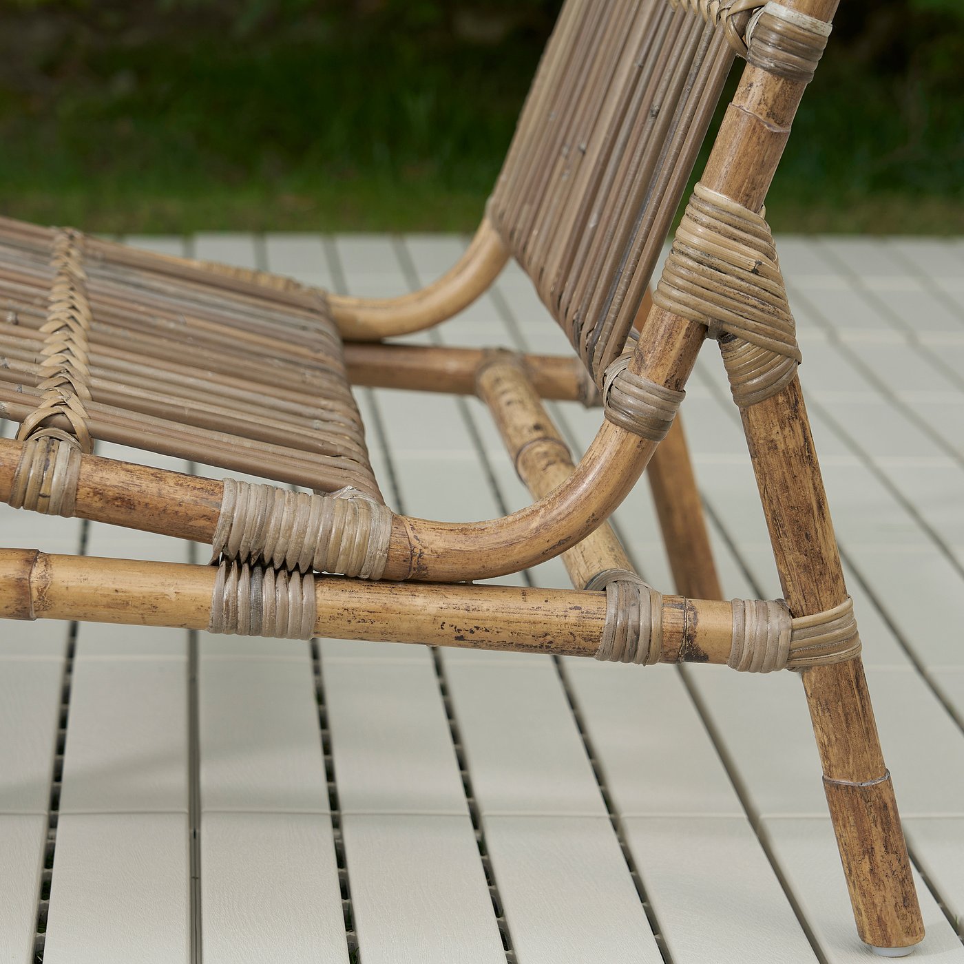 Wicker patio chair on tiled deck. Crafted with rattan and stainless steel joints, showcasing sturdy, detailed handiwork.