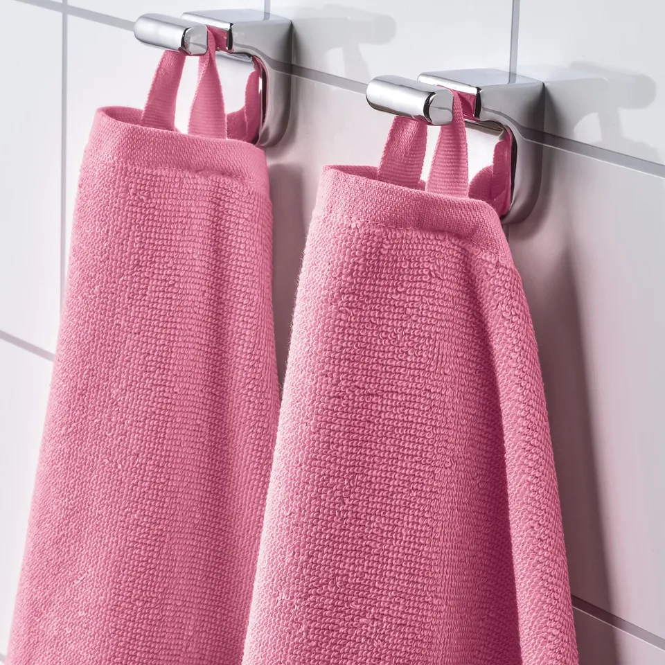 Two pink towels hang neatly from a metallic bar, displaying their soft, absorbent texture and vibrant colour.