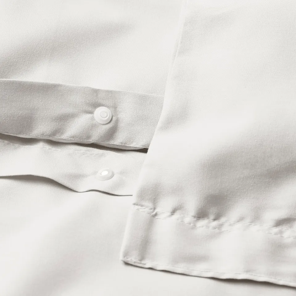 Close-up of white duvet cover press-stud closure. Fabric blend, wrinkle-resistant, smooth with fine sheen.