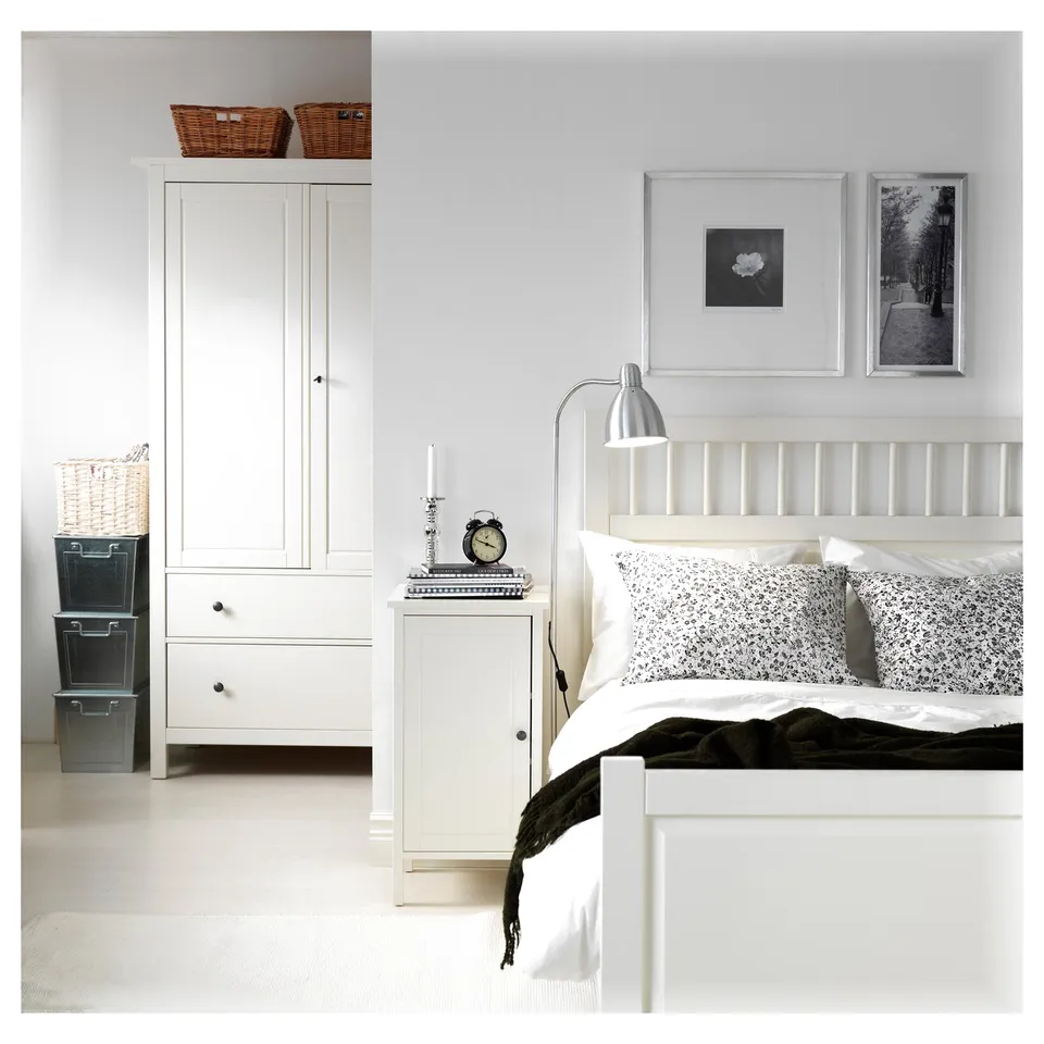 Bedroom with white furniture: bed, closet, bedside table, lamp, and wall art. Black and white theme.