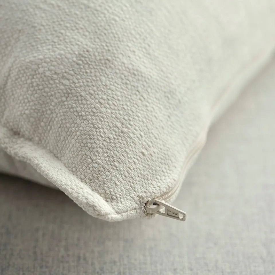 Close-up of textured off-white cushion cover with zip, showcasing high-quality fabric and precise stitching.