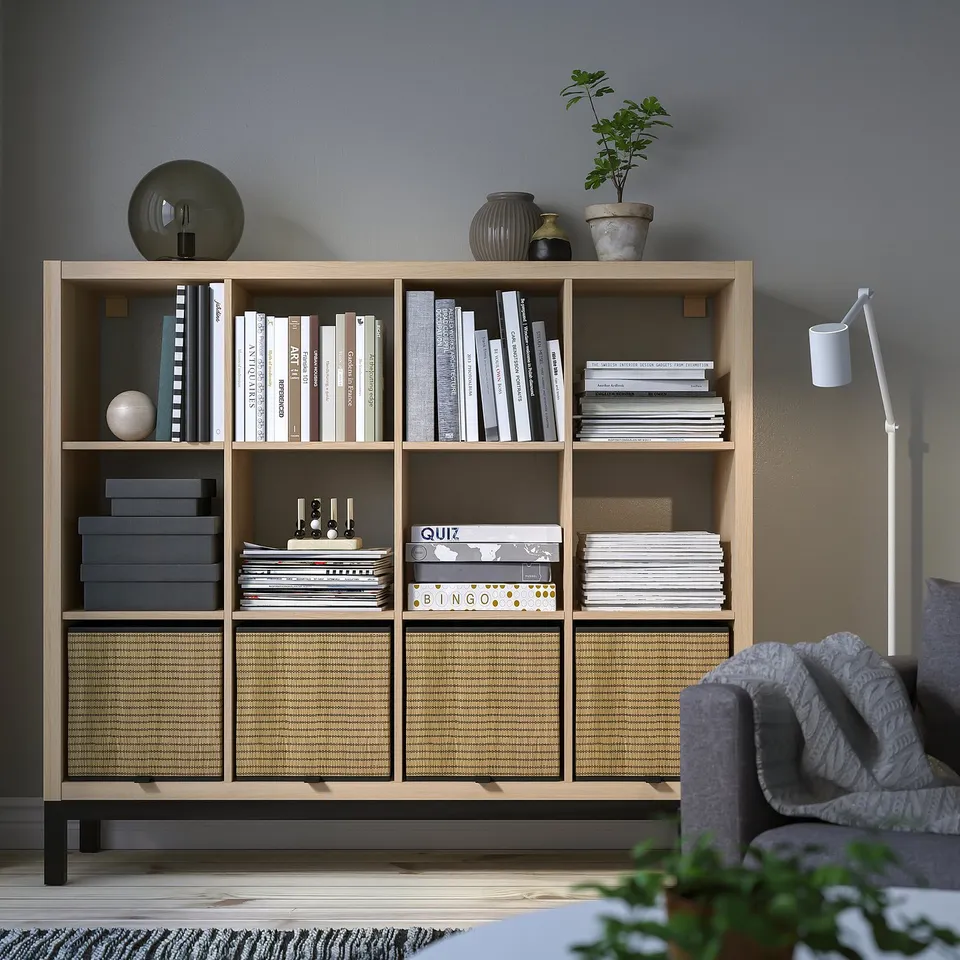 The KALLAX shelving unit, light wood, holds many books and decor items, complementing a cosy room.