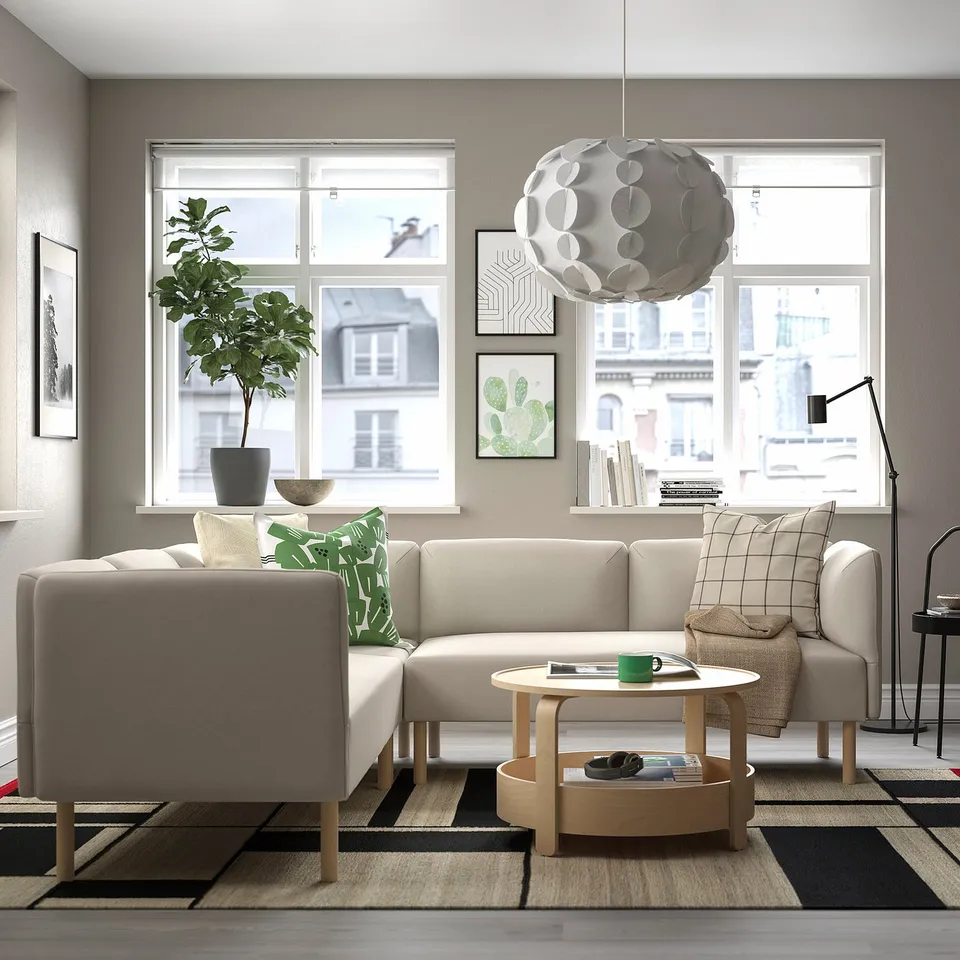 Modern living room with LILLEHEM beige modular sofa, green plant, patterned rug, wooden coffee table, and large windows.
