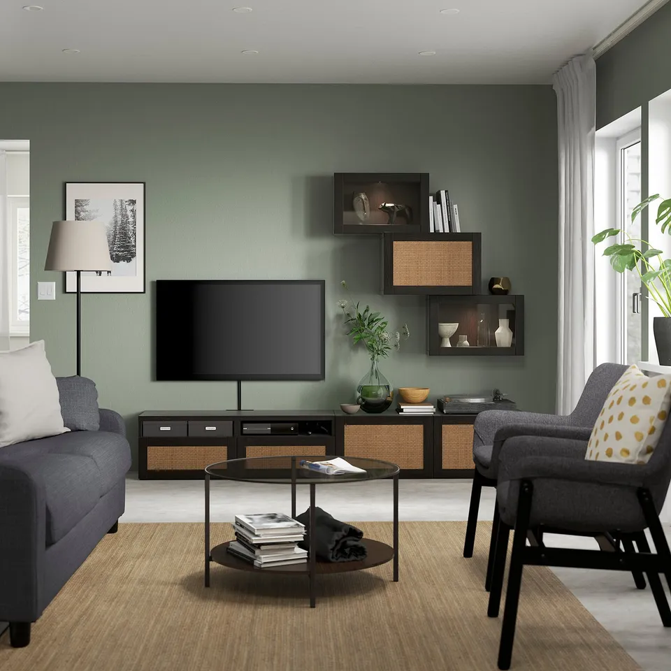 Modern living room with green walls, grey sofa, armchair, and coffee table. Tv on stand with shelves holding decor.