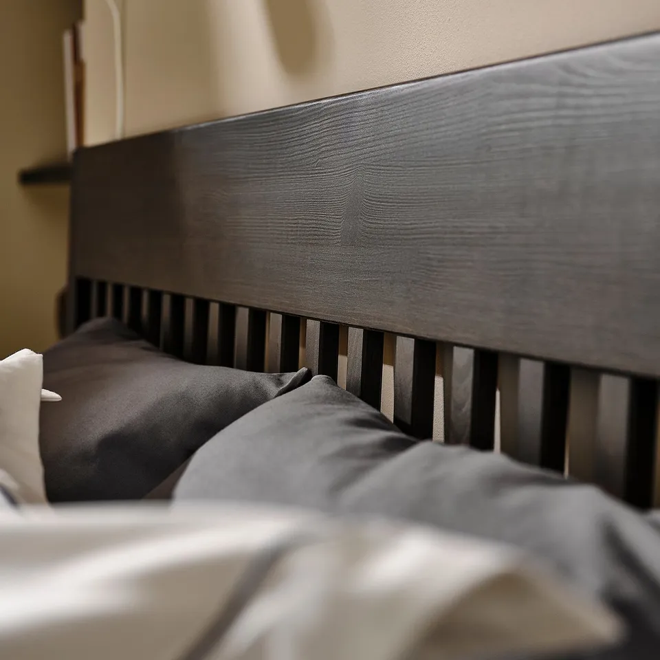 Modern bed with dark wood headboard and slatted design, neatly made with grey linens.
