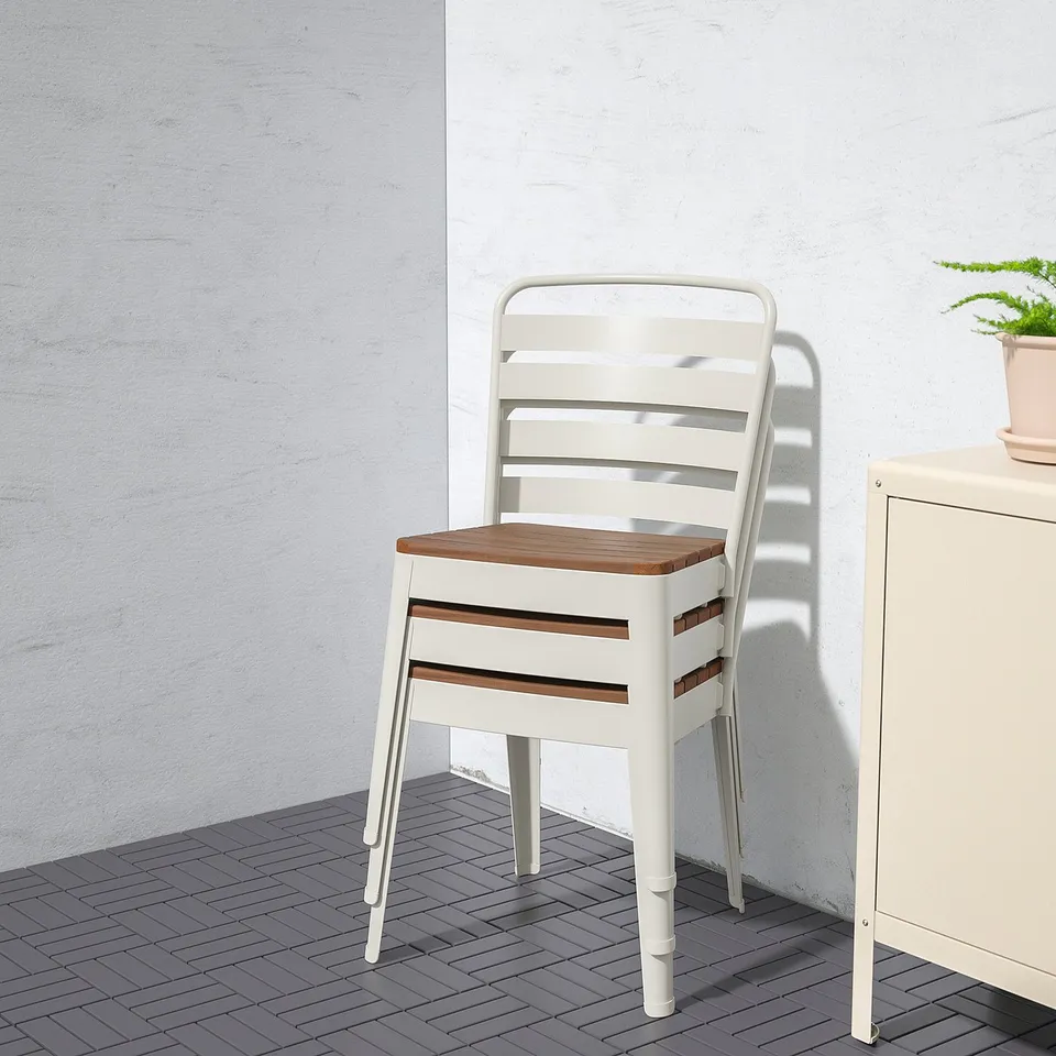 White metal chair with wooden seat against a grey wall and floor.