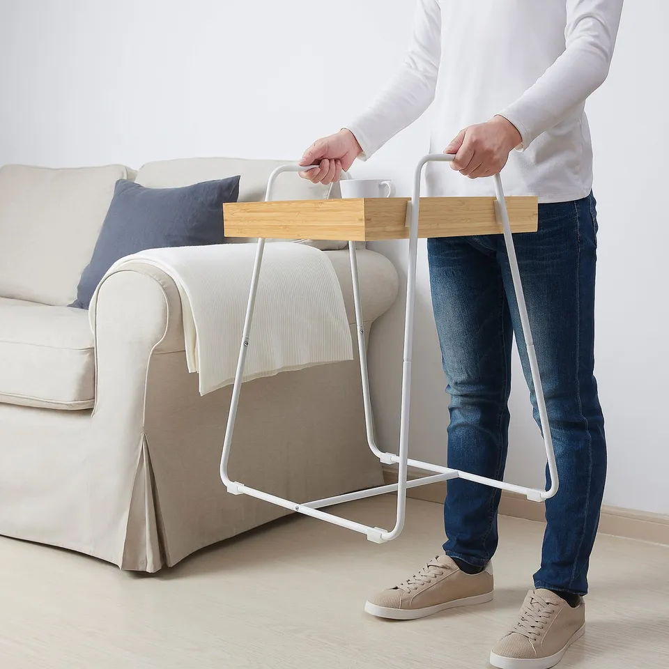 Person holding flat-packed bamboo table near beige couch.