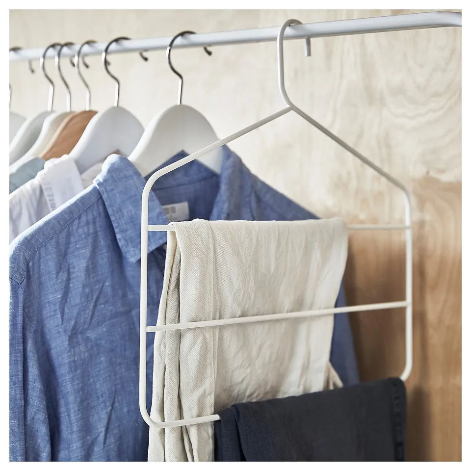 White metal closet hanger holding blue shirt and light trousers.