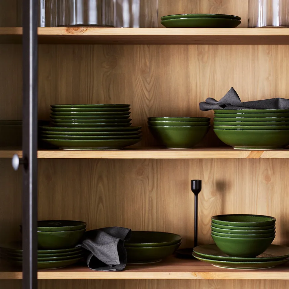 Wooden shelves with green bowls, plates, napkins, & candle for a natural table setting.