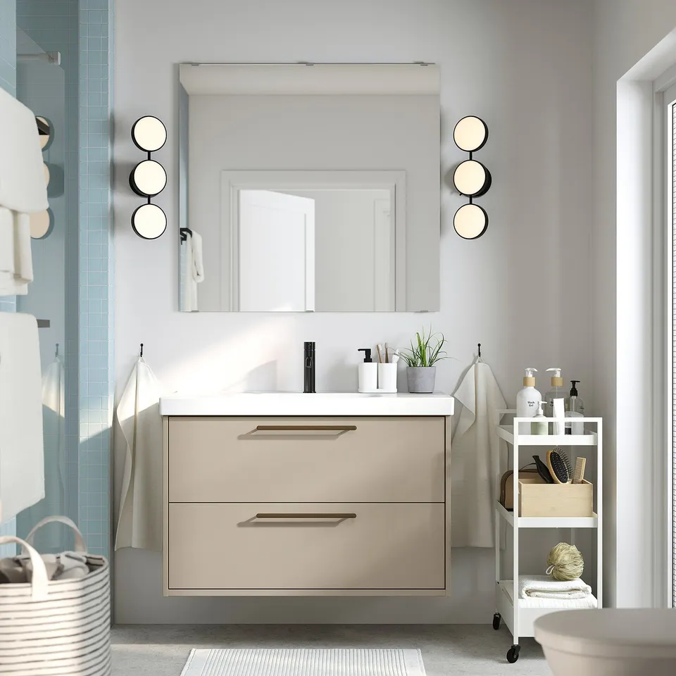 Modern beige bathroom with HAVBÄCK vanity, mirror, and lamps. Includes sink, cart, and toiletries. Light and airy.